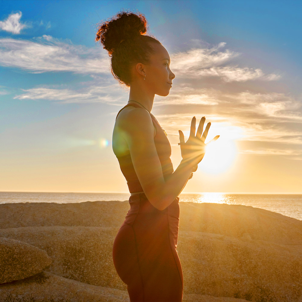 Yoga, meditation or sunset with woman in peace by the ocean, sea or beach for meditation, zen or chakra balance. Spiritual, health or fitness girl on rock or sand for mindset goal, pilates or workout.