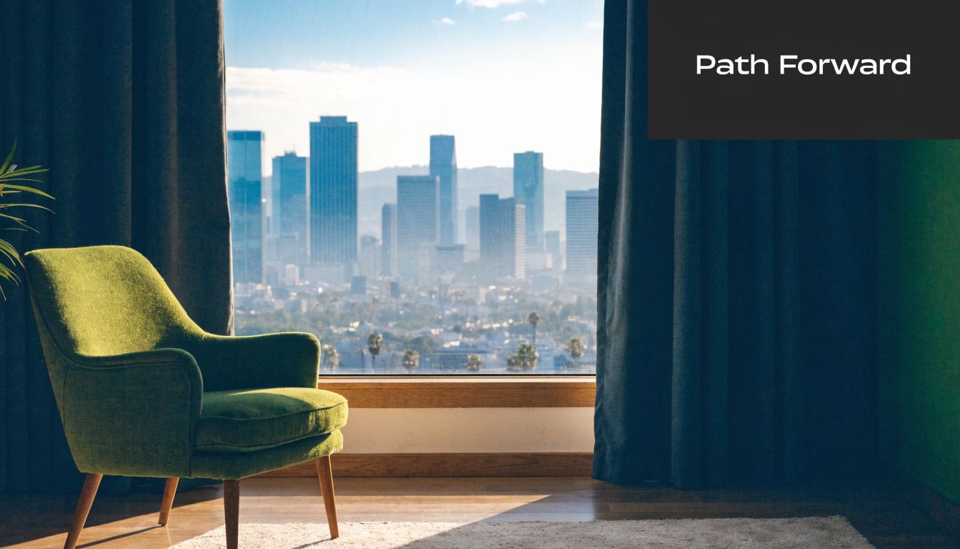A modern green armchair sits near a window overlooking a bright Los Angeles city skyline at daytime.