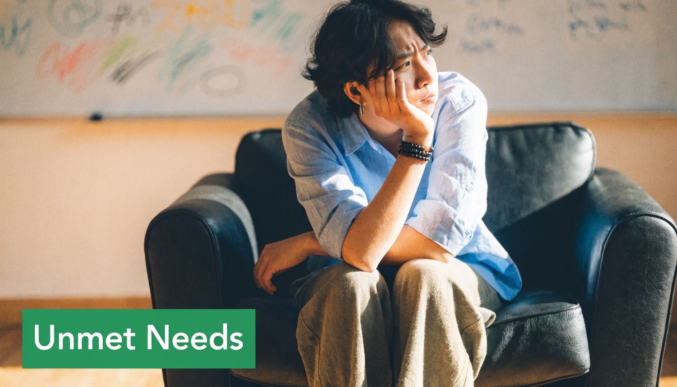 A person sitting on a dark chair looking frustrated and pensive, with the text Unmet Needs below.