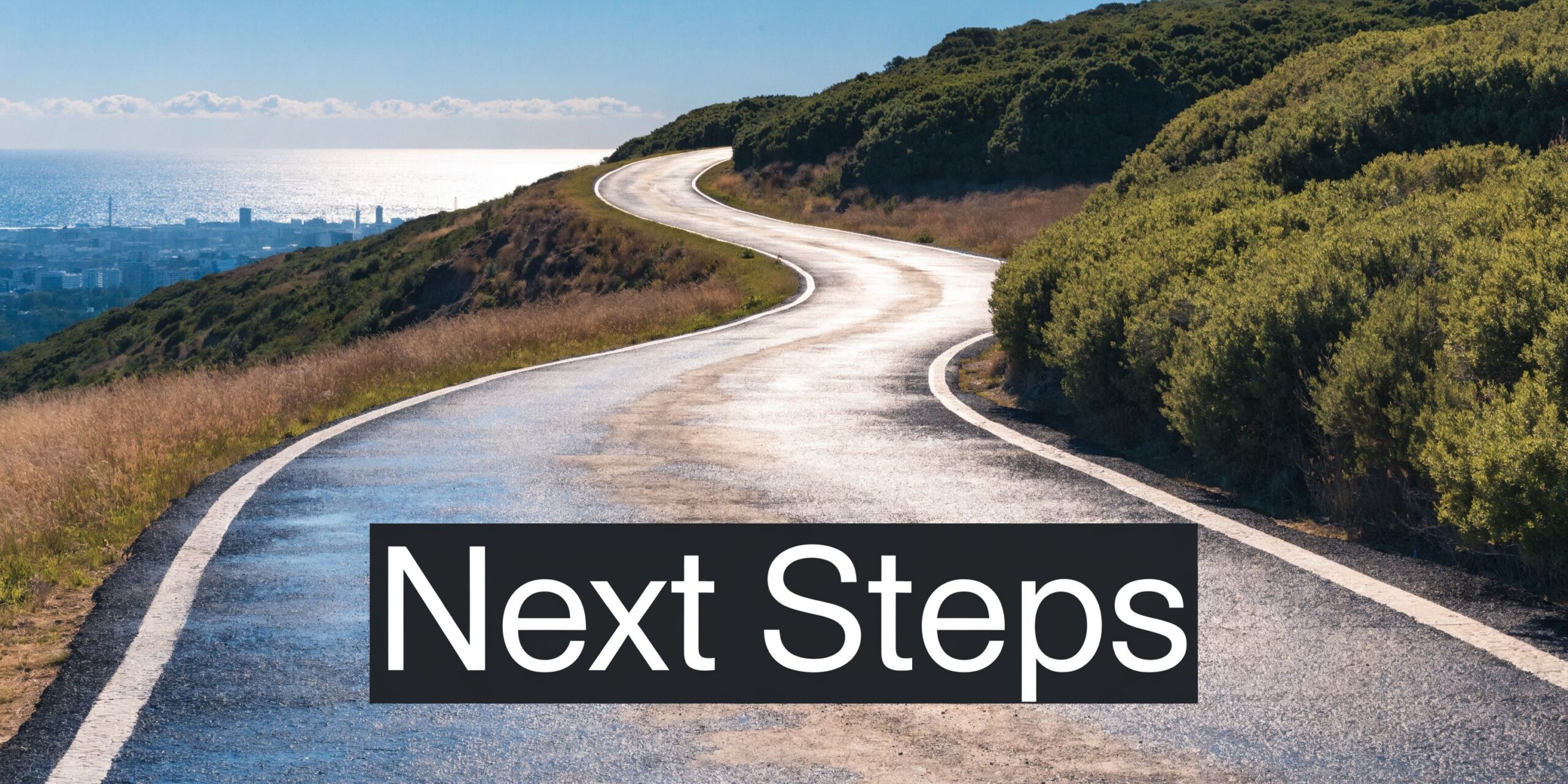 A scenic, winding road leading toward a coastal city under a clear sky on a bright day.