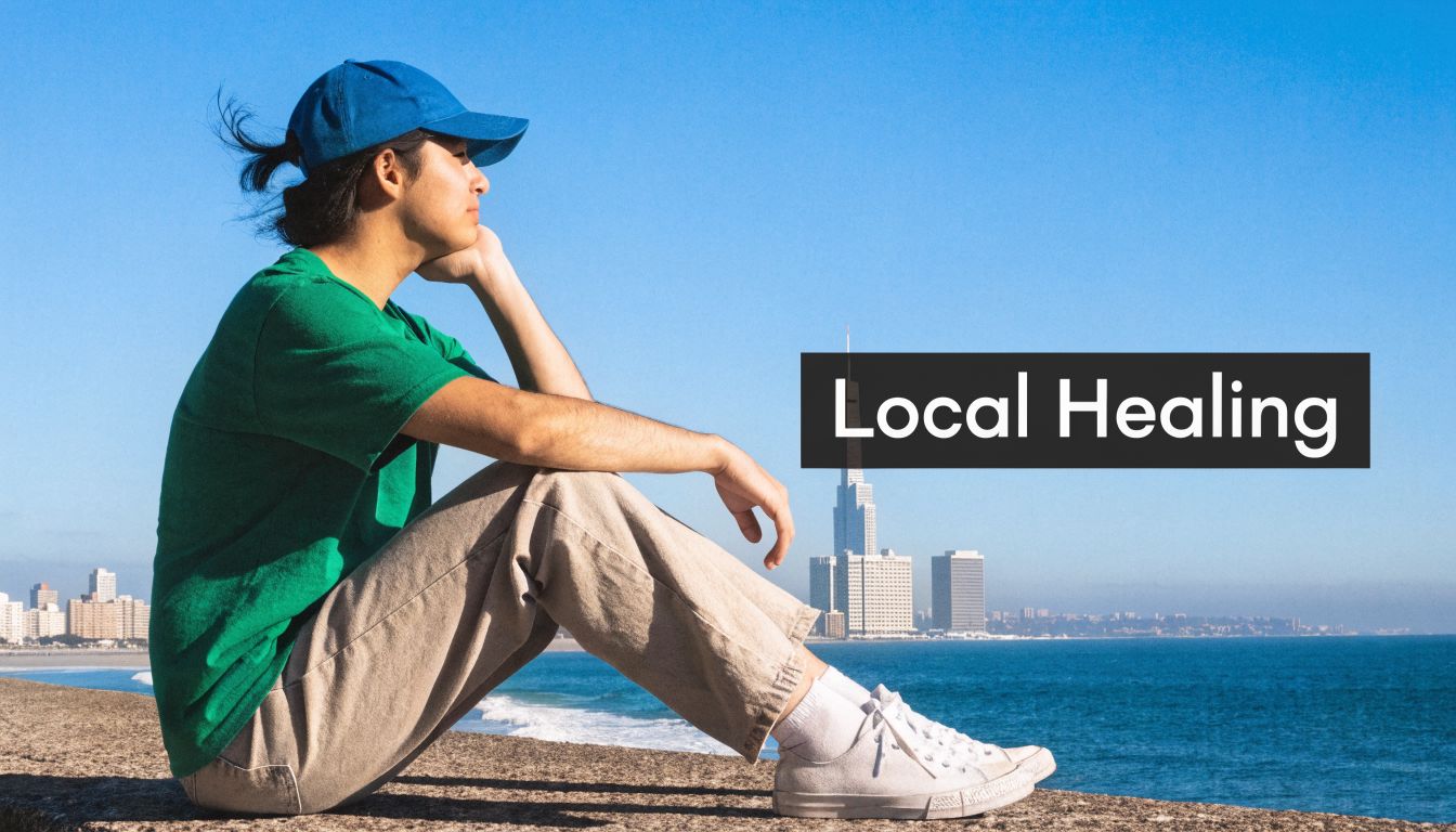A person sitting on a wall by the ocean, looking at the city skyline in the distance.