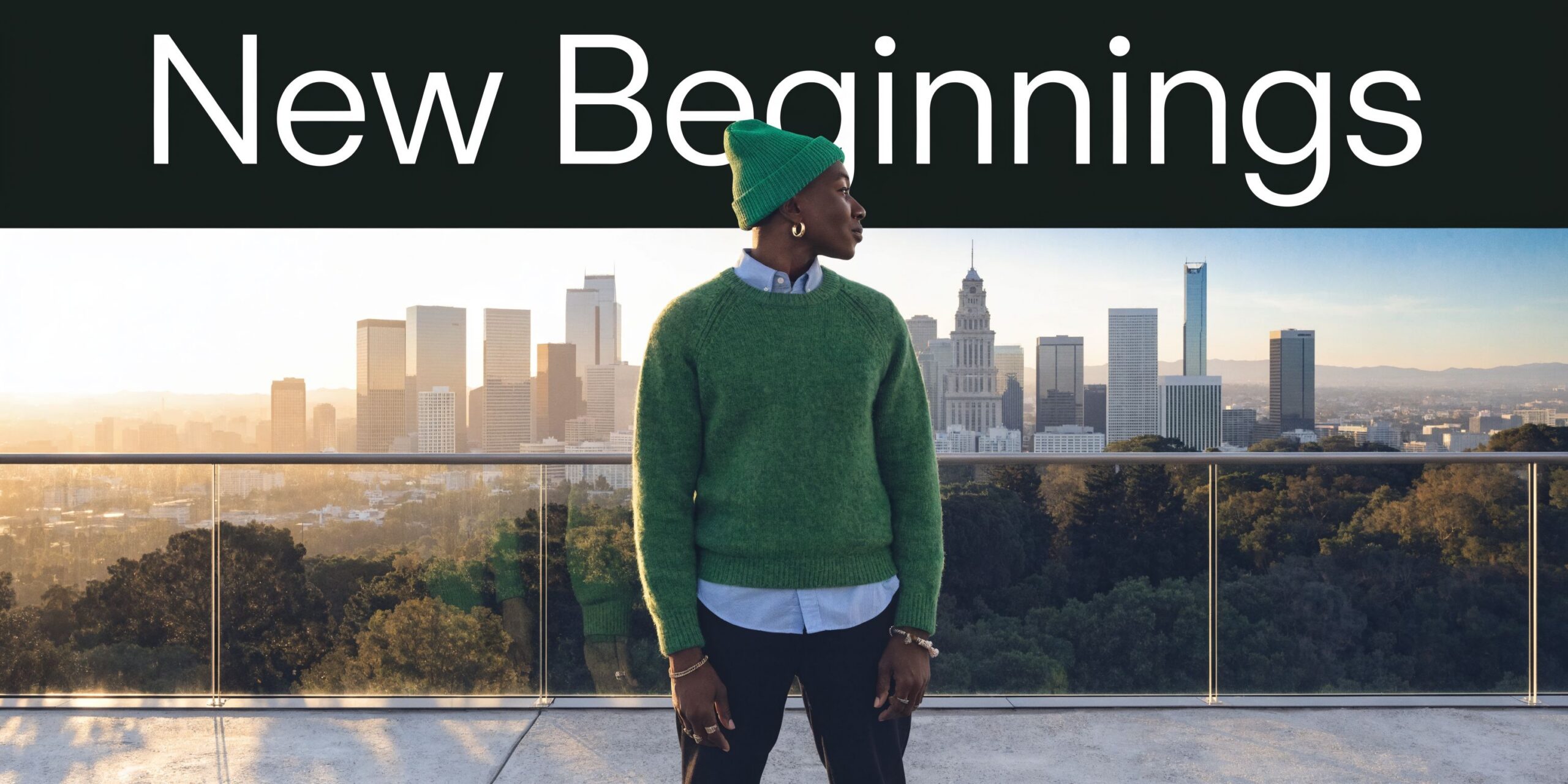 A person wearing a green sweater and beanie standing on a balcony overlooking the Los Angeles skyline.
