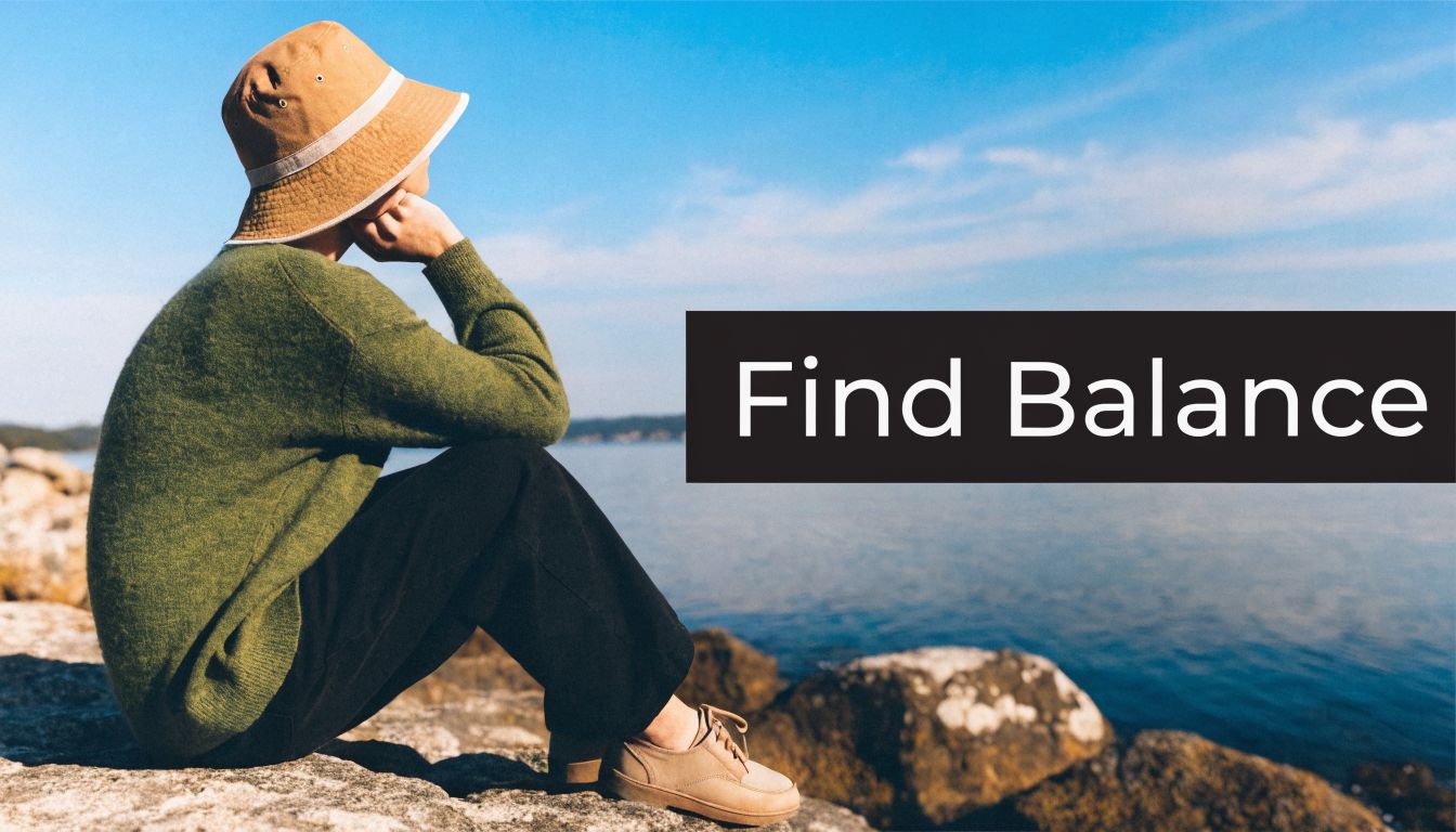 A person in a hat and sweater sits on rocks by the water, reflecting on finding balance.