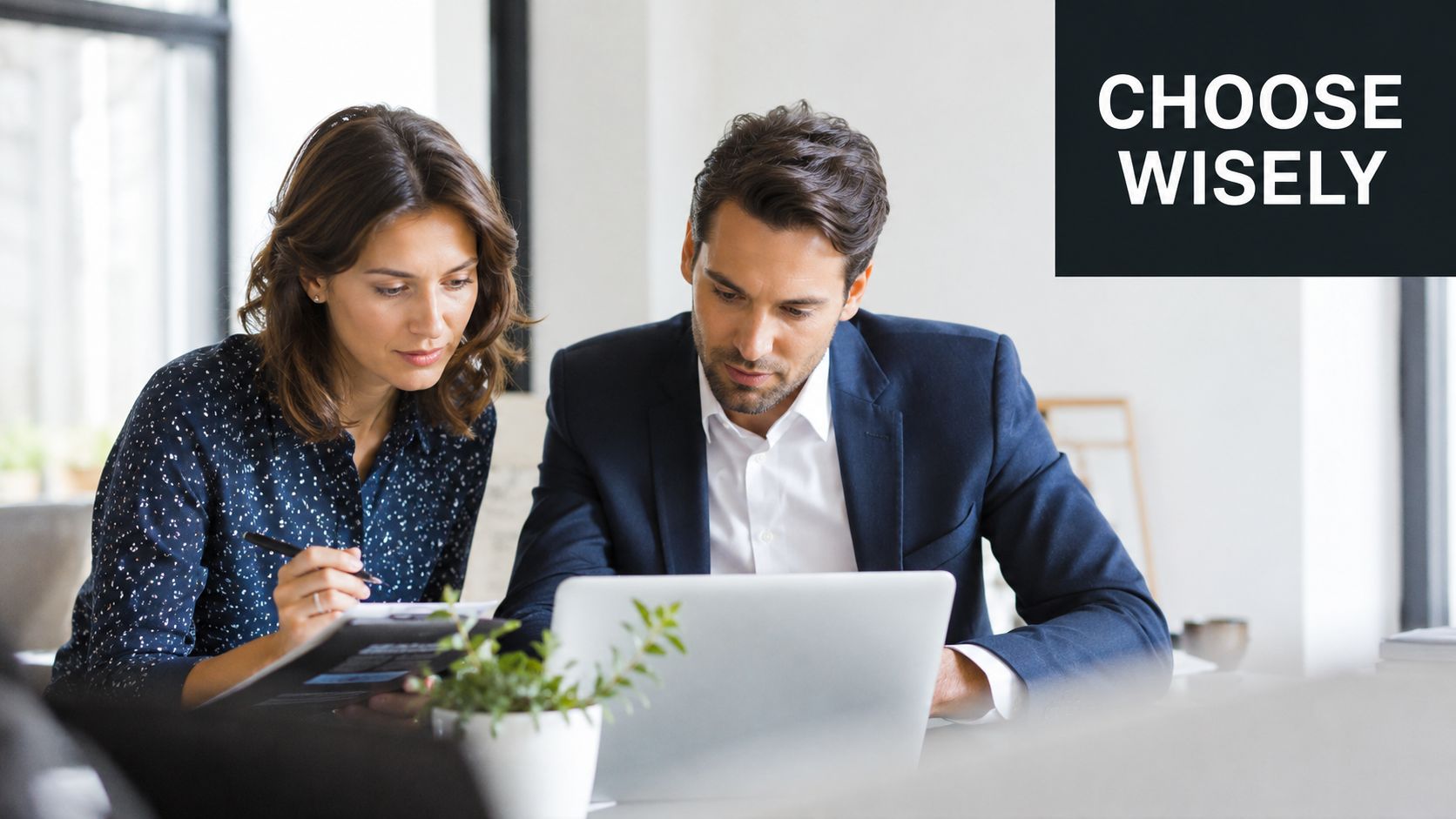 A professional man and woman working together on a laptop and documents at an office desk.